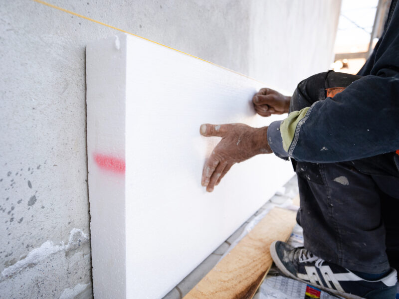 Worker placing styrofoam sheet insulation to the wall at construction site Rigid extruded polystyrene insulation board for energy saving Of Facade house renovation energy efficient